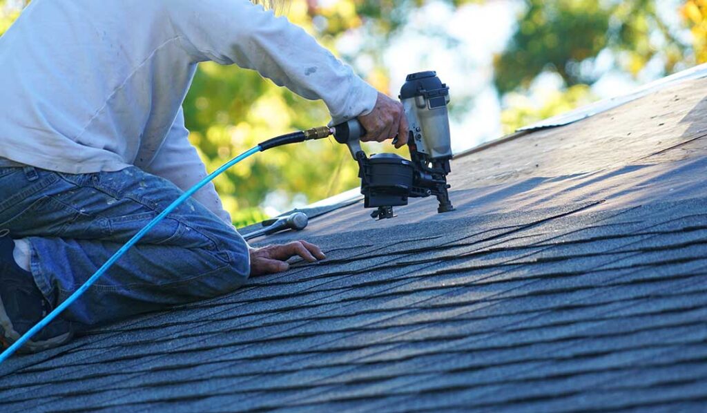 Person inspecting a pitched shingle roof with visible weather wear under partly cloudy skies.